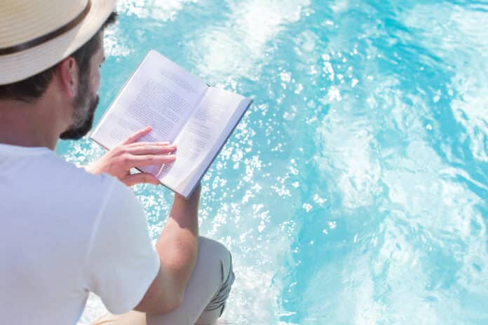 Man reading book over swimming pool
